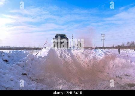 Offroad-SUV „Suzuki Escudo“ fährt im Geländewagen auf einem schneebedeckten Berg in den Wolken des farbigen braunen Rauchs im Winter auf einer kaputten Straße während des Tages. Stockfoto