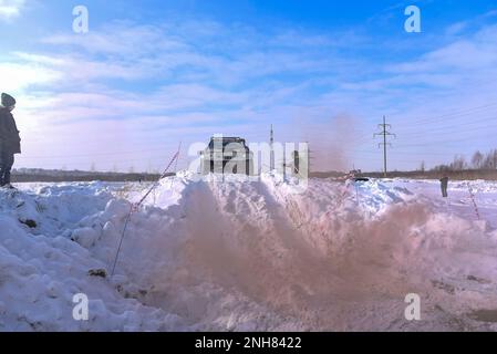 Offroad-SUV „Suzuki Escudo“ fährt im Geländewagen auf einem schneebedeckten Berg in den Wolken des farbigen braunen Rauchs im Winter auf einer kaputten Straße während des Tages. Stockfoto