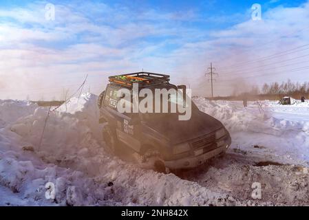 Geländewagen „Suzuki Escudo“ fährt im Geländewagen schnell auf einer verschneiten Straße im braunen Rauch und hebt die Räder eines Schneesturms. Stockfoto