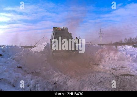 Geländewagen „Suzuki Escudo“ fährt im Geländewagen schnell auf einer verschneiten Straße im braunen Rauch und hebt die Räder eines Schneesturms. Stockfoto