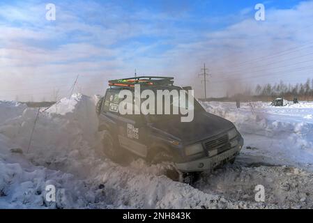 Geländewagen „Suzuki Escudo“ fährt im Geländewagen schnell auf einer verschneiten Straße im braunen Rauch und hebt die Räder eines Schneesturms. Stockfoto