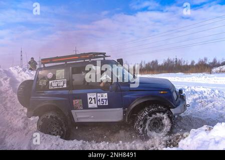 Geländewagen „Suzuki Escudo“ fährt im Geländewagen schnell auf einer verschneiten Straße im braunen Rauch und hebt die Räder eines Schneesturms. Stockfoto