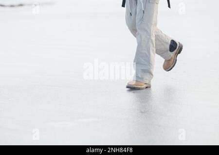 Ein bärtiger Mann mit einem Rucksack in warmer Winterkleidung läuft im Winter auf einem gefrorenen See. Das Konzept der Wanderung und des aktiven Lebensstils. Stockfoto