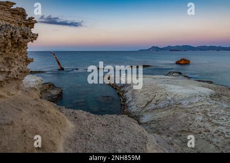 Die weiße Klippe von Sarakiniko in der Abenddämmerung mit dem Wrack eines Schiffes in der Mitte des Wassers, Milos Stockfoto