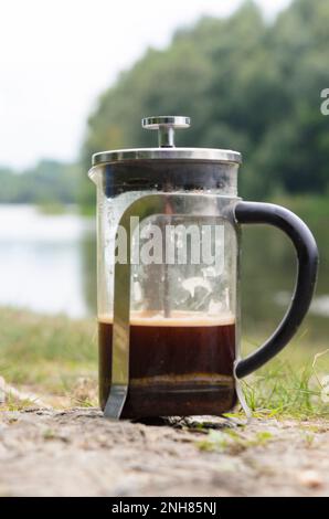 Kaffee, der in einer französischen Presse auf den Steinen des Flusses im Wald in der Nähe des Grases gebrüht wird. Stockfoto