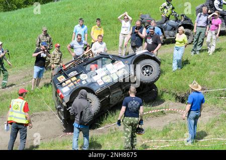 Zuschauermassen schauen auf das Auto „Suzuki Jimny“, das hoch erhöhte Felgen am Eingang zum Berg auf dem Wettkampf in Nowosibirsk ist Stockfoto