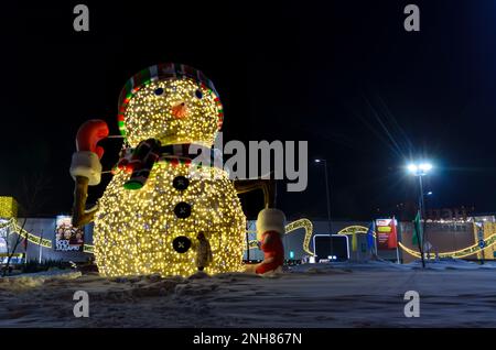 Frau, die im Winter einen Mann im Laden „IKEA“ fotografiert, in der Nähe eines glühenden Schneemanns. Weihnachtsdekoration der Straßen in der Nähe des Ladens „Mega“ Stockfoto