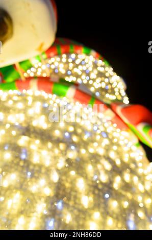 Leuchtender Schneemann auf dem Boden mit rot-grün-weißem Schal und Kappe der Lampe am Himmel. Silvesterabend und Straßendekoration an Weihnachten. Stockfoto