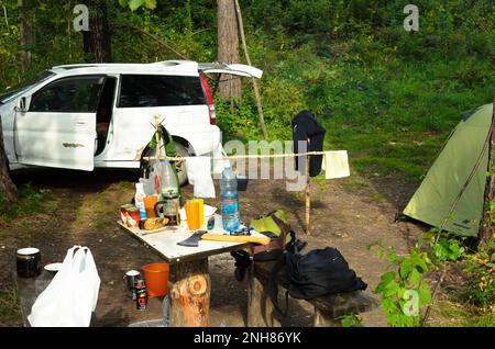 Die Marke „Honda HR-V“ steht am Campingtag in den Wäldern in der Nähe des Zelts „Nordway“ und eines Holztisches mit Essen, Wasser, Axt und Rucksäcken in Altai Stockfoto