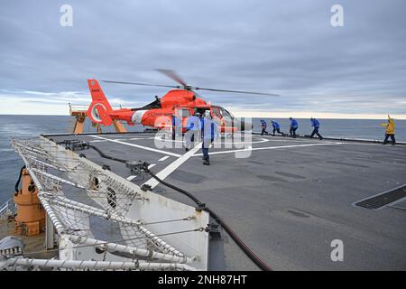 EIN US-AMERIKANISCHER Coast Guard Air Station Kodiak MH-65 Dolphin Helikopter landet, während Coast Guard Cutter Healy Crewmitglieder sich nähern und am 21. Juli 2022 in der Nähe des Polarkreises Verzurrungen installieren. Schulungen werden routinemäßig durchgeführt, um die Qualifikation der Besatzung an Bord beider Anlagen zu erhalten und die Kenntnisse in einer Vielzahl von Entwicklungen zu erhalten. USA Hilfsfoto der Küstenwache von Deborah Cordone. Stockfoto