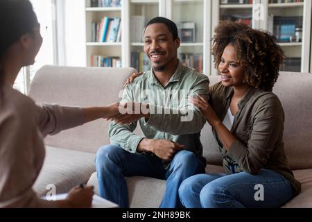 Positiv lächelndes afroamerikanisches Paar, das Therapeuten die Hand schüttelt Stockfoto