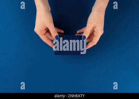 Mini-Videokassette in weiblichen Händen vor klassisch blauem Hintergrund Stockfoto