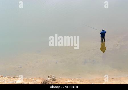 Ein Fischer in einer Jacke steht mit einer Angelrute im Wasser des Flusses und fängt Fische in Russland. Stockfoto