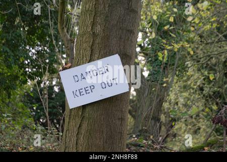 Das Schild mit dem Hinweis auf Gefahr ist an einen Baumstamm genagelt Stockfoto