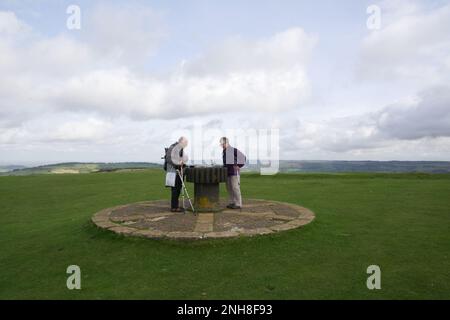 Zwei Erwachsene neben dem Toposkop auf dem Gipfel von Cleeve Hill, die Cotswolds, Gloucestershire, England, Großbritannien Stockfoto