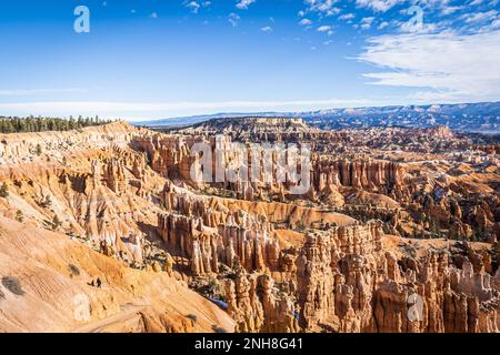 Der Bryce Canyon ist mit frisch gefallenem Schnee und fernen Bergen und leuchtend farbigen orangefarbenen Klippen geschmückt. Stockfoto