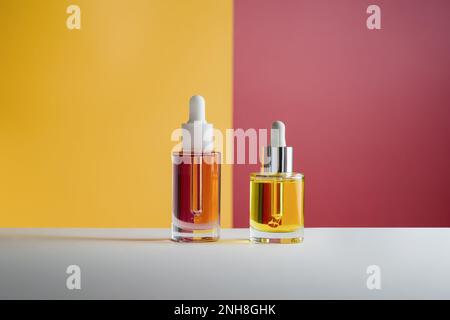 Pinkfarbenes und gelbes Gesicht und Haaröl in Glasflaschen mit Pipettierhelfer auf leuchtend orangefarbenem und rotem Hintergrund. Unauffällige Schönheits-Selbstpflegefotografie Stockfoto