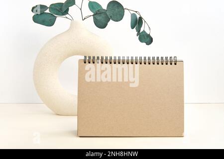 Leere Grußkarte, Einladungsmodell. Vorderansicht. Eukalyptusbranche in moderner Keramikvase auf dem Tisch. Speicherplatz kopieren. Papiermodell. Minimaler Br Stockfoto