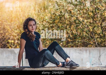 Ruhende Teenagerin, die auf dem Boden sitzt. Traumhafte Augen. Hintergrund bei Sonnenuntergang. Stockfoto