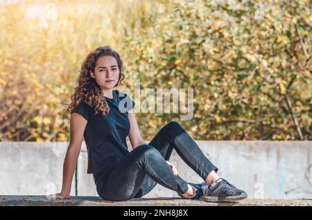 Sportliche Frau, die auf dem Boden sitzt. Traumhafte Augen. Hintergrund bei Sonnenuntergang Stockfoto