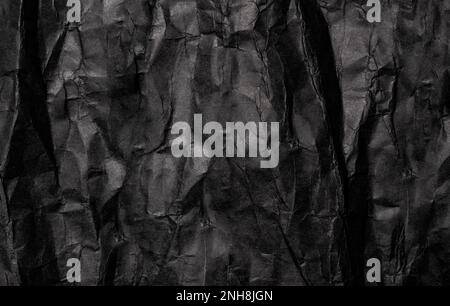 Schwarze zerknitterte Papierstruktur bei schwachem Hintergrund. Ein alter grunge schwarzer Papierhintergrund. Zerknittertes Papier. Kopierraum für Text, Design-Kunstwerke. Stockfoto