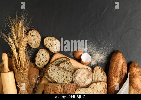Man kann Multi-Grain-Sauerteigbrot und geschnittenes Baguette mit Weizenmehl auf schwarzem Steinhintergrund, hausgemachtes Bäckereikonzept, zubereiten Stockfoto
