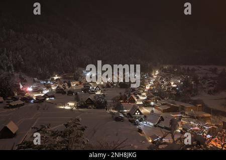 Lichter aus dem traditionellen Bergdorf durchdringen Schnee und Nebel bei Nacht Stockfoto