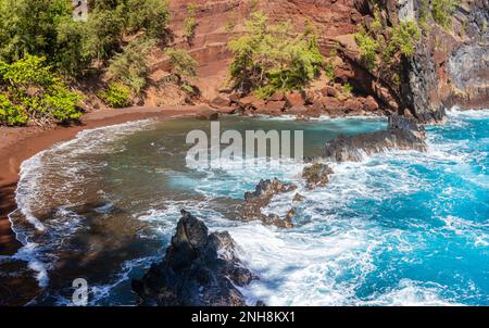 Roter Sand und blaue Wellen am Kaihalulu Beach, Hana, Maui, Hawaii, USA Stockfoto