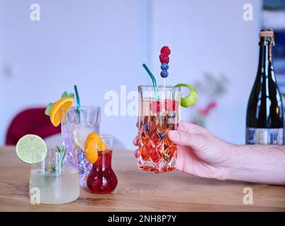 Berlin, Deutschland. 18. Februar 2023. Illustration: Alkoholfreie Cocktails ( Limello Spritz, Gin Tonic, Aperitivo ) liegen auf einem Tisch, während ein Mann die Aperol Wild Berry nimmt. Im Hintergrund eine Flasche Sekt mit null Prozent Alkohol. Kredit: Annette Riedl/dpa/Alamy Live News Stockfoto