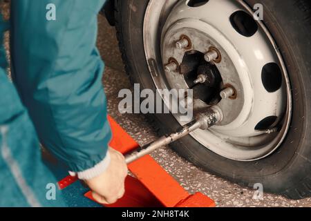 Der Mensch wechselt im Autodienst das Rad. Professioneller Automechaniker im Overall entfernt das Rad aus dem Lkw in der Garage. Authentischer Workflow... Stockfoto