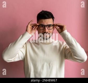 Porträt eines bärtigen Mannes, der eine Brille anzieht und beim Posen aufmerksam in die Kamera schaut Stockfoto