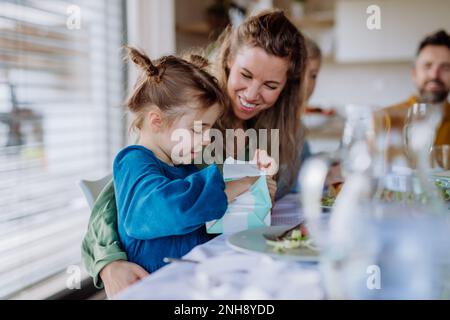 Ein kleines Mädchen, das beim Familienessen ein Geschenk auspackt. Stockfoto