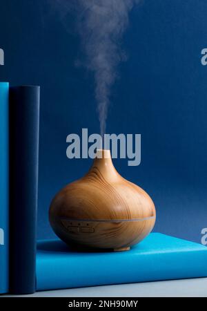 Holzduft auf dem Schreibtisch mit natürlichen Ölen, Essenz-Dampf, blaue und türkisfarbene Bücher Stockfoto