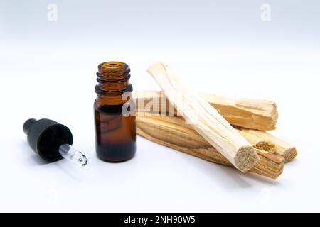Palo Santo (Heiliger Strohsack), ätherischer Ölextrakt Essense in einer Flasche mit Palo Santo-Stäbchen daneben. Nahaufnahme isoliert auf weißem Hintergrund. Stockfoto