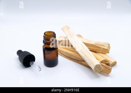 Palo Santo (Heiliger Strohsack), ätherischer Ölextrakt Essense in einer Flasche mit Palo Santo-Stäbchen daneben. Nahaufnahme isoliert auf weißem Hintergrund. Stockfoto