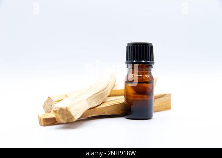 Palo Santo (Heiliger Strohsack), ätherischer Ölextrakt Essense in einer Flasche mit Palo Santo-Stäbchen daneben. Nahaufnahme isoliert auf weißem Hintergrund. Stockfoto