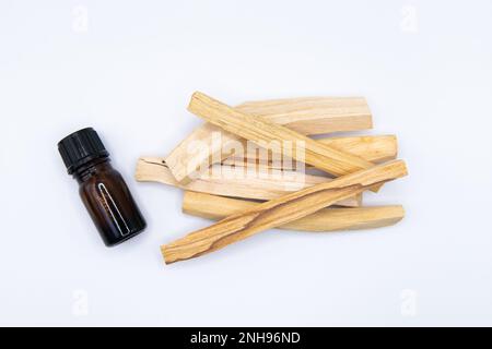 Palo Santo (Heiliger Strohsack), ätherischer Ölextrakt Essense in einer Flasche mit Palo Santo-Stäbchen daneben. Nahaufnahme isoliert auf weißem Hintergrund. Stockfoto