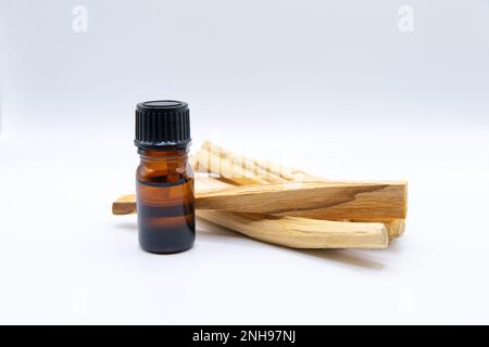 Palo Santo (Heiliger Strohsack), ätherischer Ölextrakt Essense in einer Flasche mit Palo Santo-Stäbchen daneben. Nahaufnahme isoliert auf weißem Hintergrund. Stockfoto