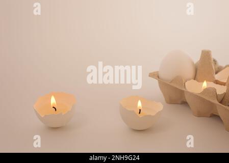Osterkarte mit Kerzen in Eierschale und Tablett mit weißem Ei auf hellem Hintergrund. Urlaub wird mit Ihren eigenen Händen gemacht. Kreativer Ansatz. Bereich Kopieren Stockfoto