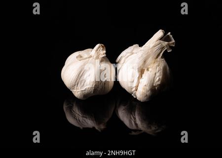 Getrocknete Knoblauchknollen auf schwarzem reflektierendem Hintergrund Stockfoto