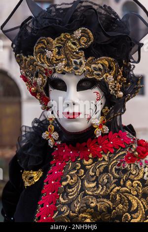 Karnevalsbesucher gekleidet in prächtigen rot-goldenen Kostümen und Maske während des Karnevals 2023 in San Polo, Venedig, Italien im Februar Stockfoto