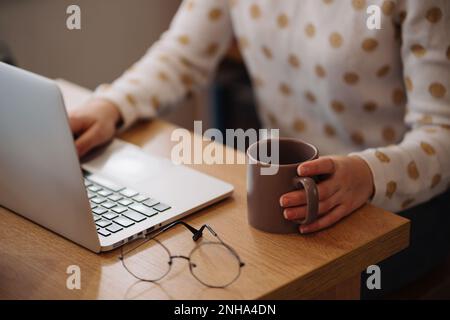 Frau, die an einem Laptop arbeitet und eine Tasse hält Stockfoto