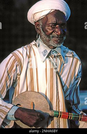 Marokko. Marrakesch. Gnawa Stammesmann. Ein Straßenmusiker, der mit dem Streichinstrument Guembri spielt. Stockfoto