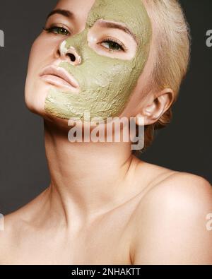 Schöne Frau, Die Grüne Gesichtsmaske Anwendet. Schönheitsbehandlungen. Close-up Portrait of Spa Girl Tragen Sie Clay Gesichtsmaske auf grauem Hintergrund. Stockfoto