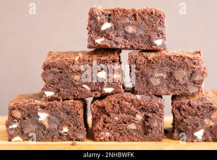 Eine Charge frisch gebackener dreifach-Schokoladen-Brownies auf einem hölzernen Servierbrett. Die Brownies sind noch warm und klebrig. Ein Genuss Stockfoto