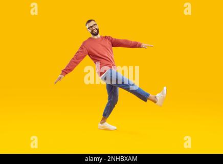 Ein fröhlicher und witziger junger Mann in Jugendkleidung tritt im Studio auf orangefarbenen Hintergrund. Stockfoto