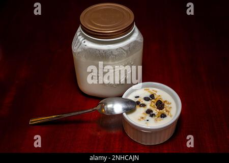 Natürlicher Kefir-Joghurt in weißem Topf mit Haferflocken, Rosinen und Honig Stockfoto