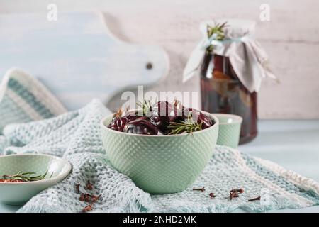 Marinierte Pflaumen mit Gewürzen im Glasgefäß auf dem Küchentisch Stockfoto