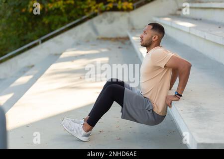 Junger afroamerikanischer Sportler, der im Stadion auf Betontreppen trainiert. Squats, schüttelt die Hände. Stockfoto