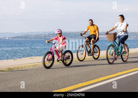 Mutter, Vater und Kind haben Spaß auf dem Radweg am Meer. Fahrradtour an der Küste für Familien. Stockfoto